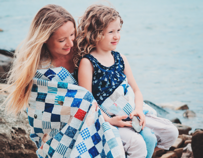 Woman and child wrapped up in a quilt on the beach