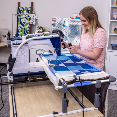 Quilter using a domestic sewing machine for longarm quilting on the Cutie Tabletop Fabric Frame