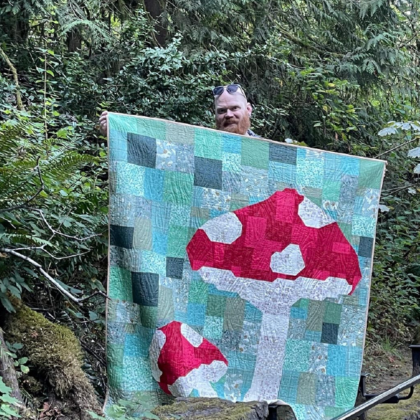 Chris holding up a patchwork mushroom quilt.